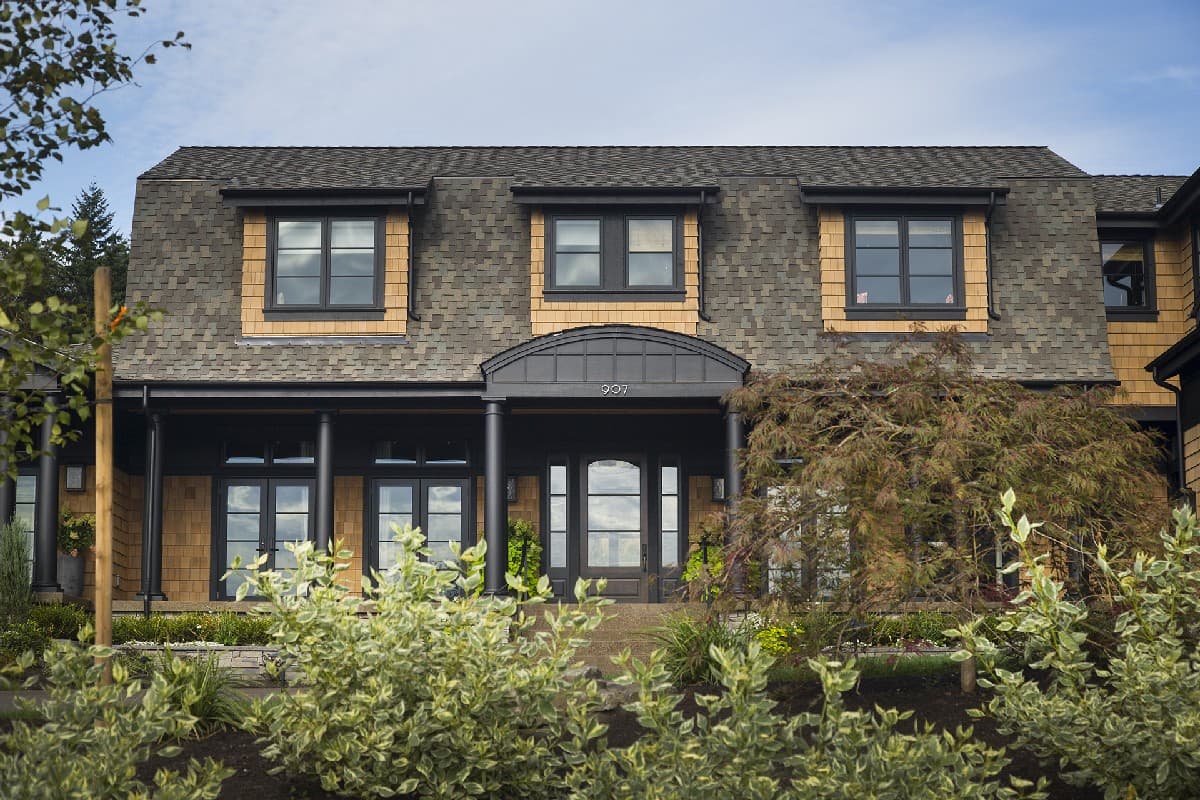 House plan exterior: Two-story structure with a covered porch, dormer windows, and wood shake siding.