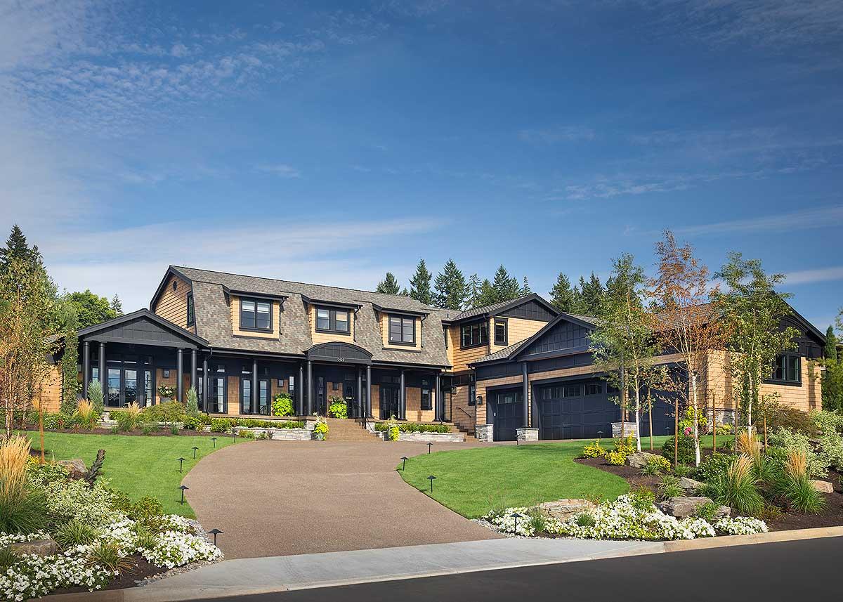 House plan exterior: Large two-story dwelling with gambrel roof, covered porch supported by columns, and attached three-car garage.