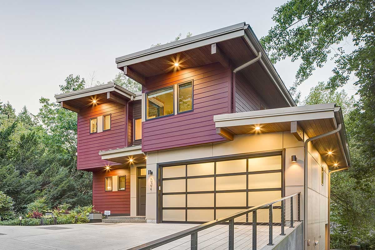 Modern house plan exterior with burgundy siding, cantilevered sections, exposed wood soffits, and frosted glass garage door.