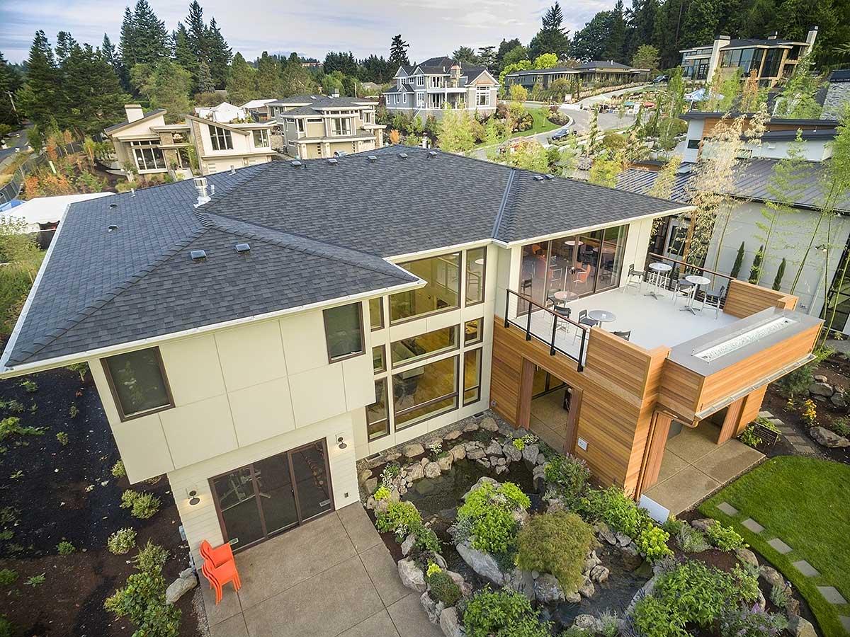 Modern house plan exterior with large windows, a multi-level roof, and a wood-clad upper deck with outdoor seating.