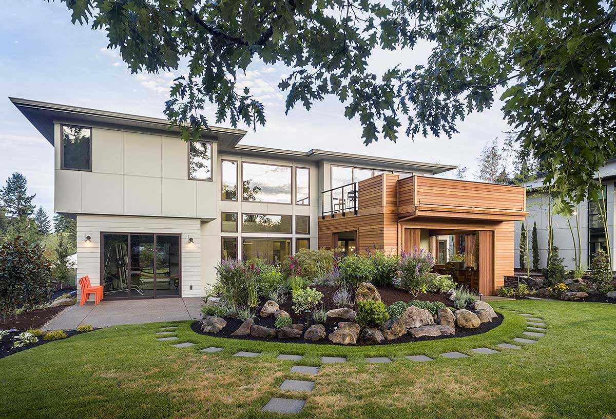 Modern house plan exterior with cantilevered second story, extensive windows, wood siding accents, and a raised deck.