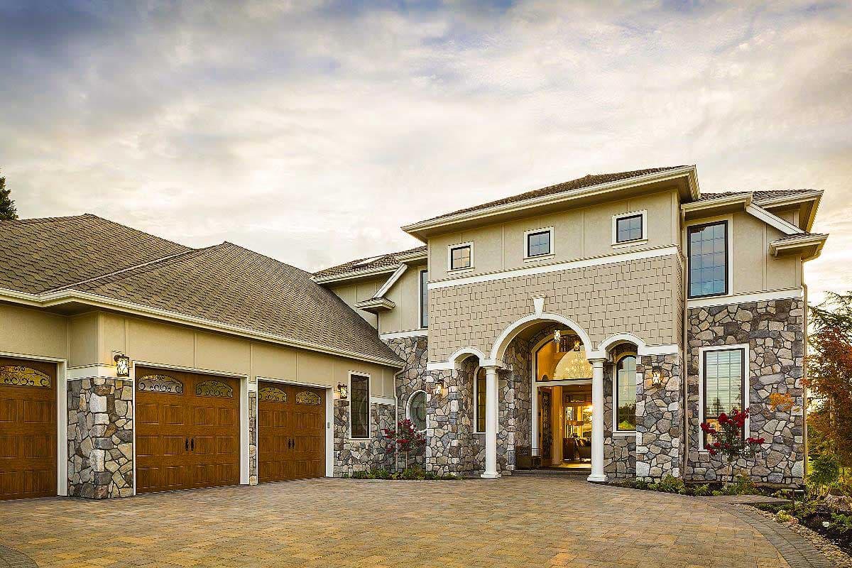 House plan exterior with a multi-level roof, stone facade, arched entryway with columns, and a three-car garage.