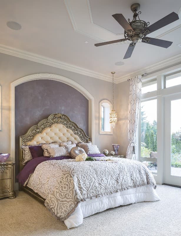 Bedroom with tufted headboard, ornate bed frame, ceiling fan, and French doors opening to an outdoor patio.