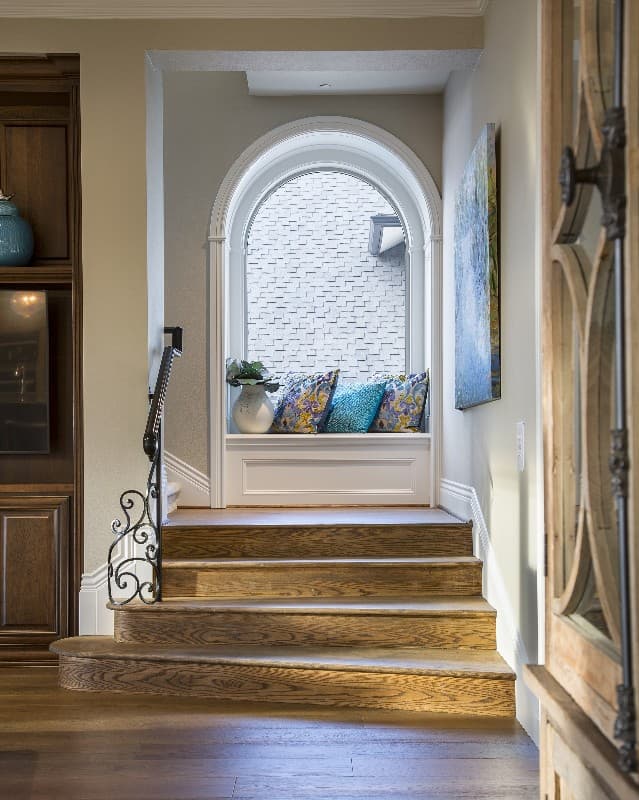 Interior view showing a wooden staircase leading to a landing with an arched window and built-in bench seating.