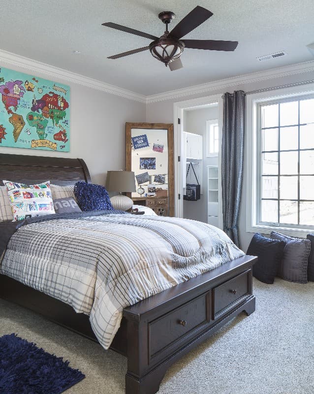 Bedroom with a dark wood bed, plaid bedding, and a world map artwork. Features a ceiling fan and large windows.