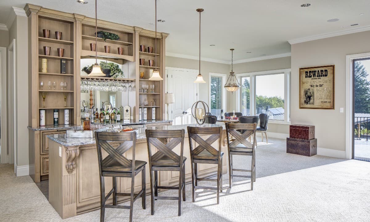Interior view of a finished basement bar area with granite countertop, built-in shelving, and bar stools. Dining area visible.