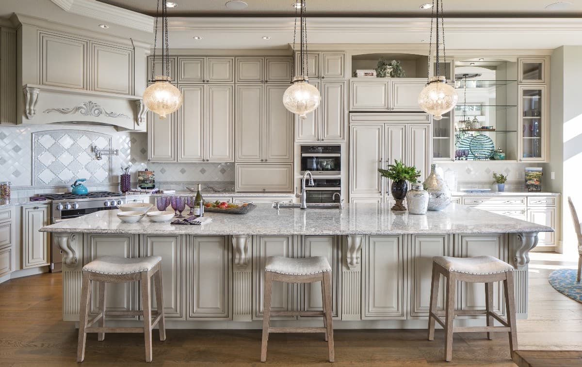 Kitchen with cream-colored cabinetry, large island with seating, gas range, and pendant lighting.