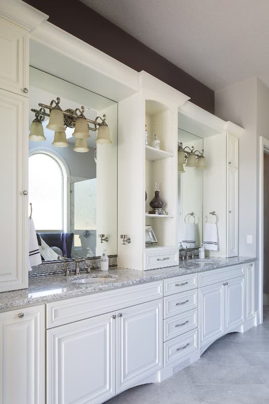 Bathroom vanity with dual sinks, granite countertops, arched mirror, and traditional white cabinetry.