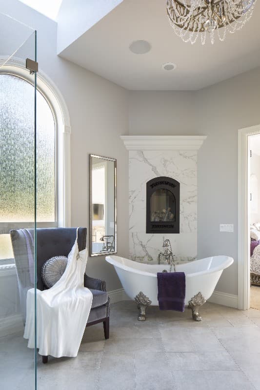 Bathroom with clawfoot tub, marble fireplace surround, vaulted ceiling, skylight, and arched window.