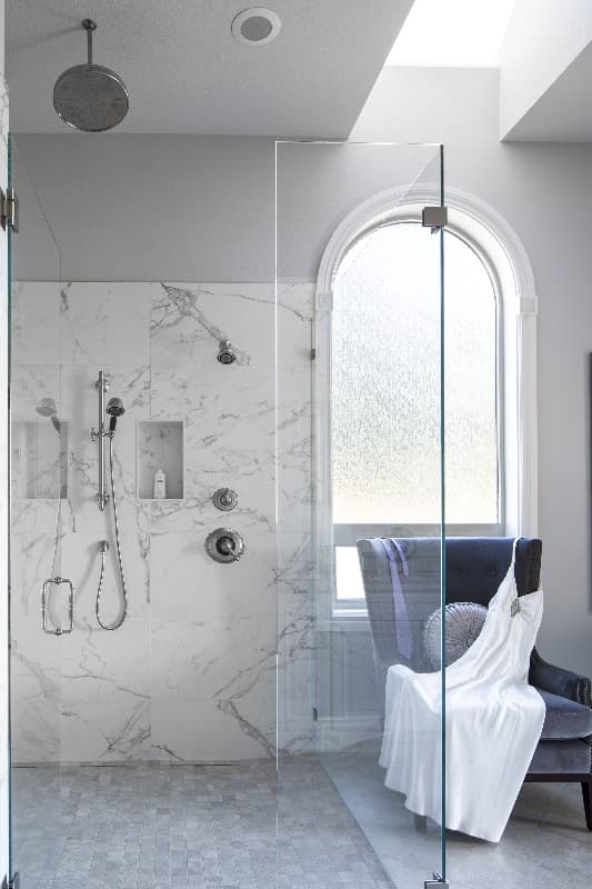 Bathroom with marble tile shower, dual shower heads, and arched window with frosted glass.