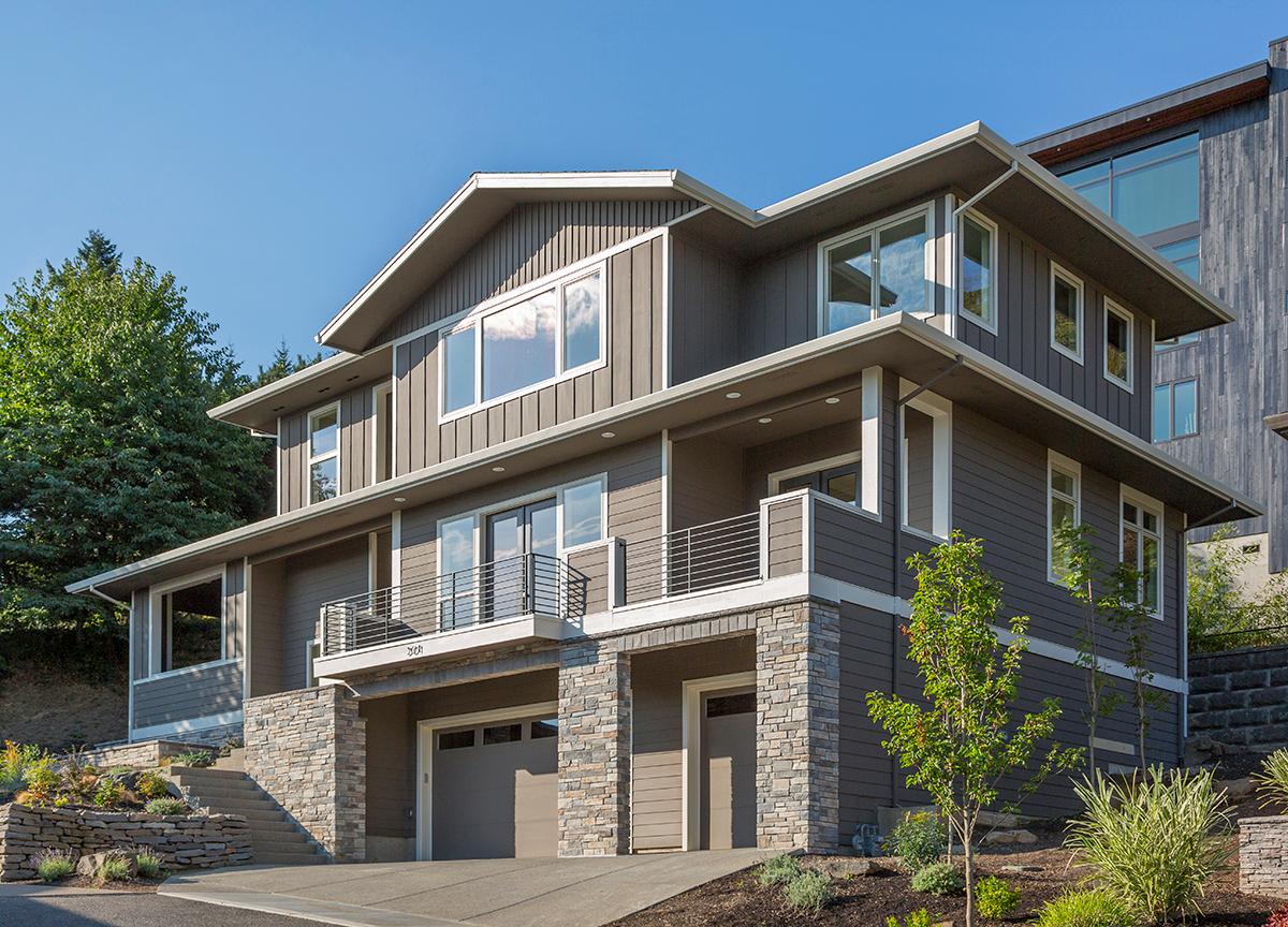 Modern two-story house plan exterior with stone accents, multiple gables, balconies, and a double garage.