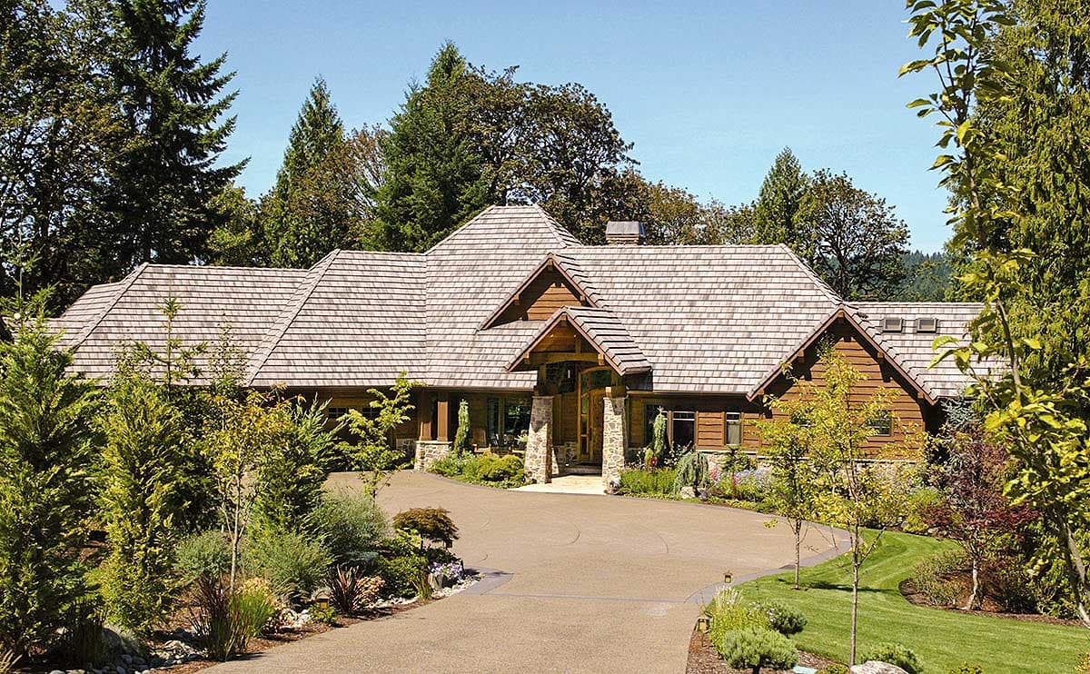 House plan exterior: Wood-sided, multi-gable roof, single-story residence with stone-clad entryway and attached garage.