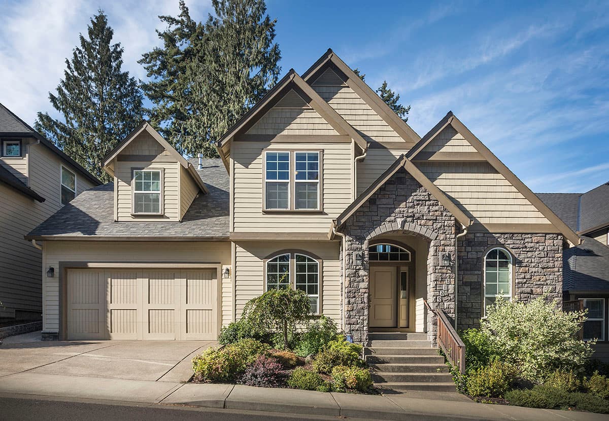 House plan exterior: Two-story home with stone-clad arched entryway, multi-material siding, dormers, and attached two-car garage.