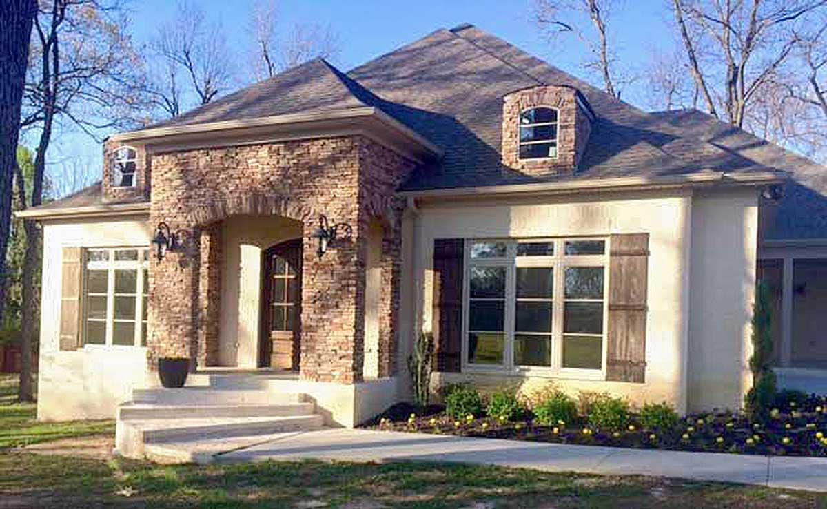 House plan exterior with stone accents on arched entryway, dormer window, and multi-pane windows with shutters.