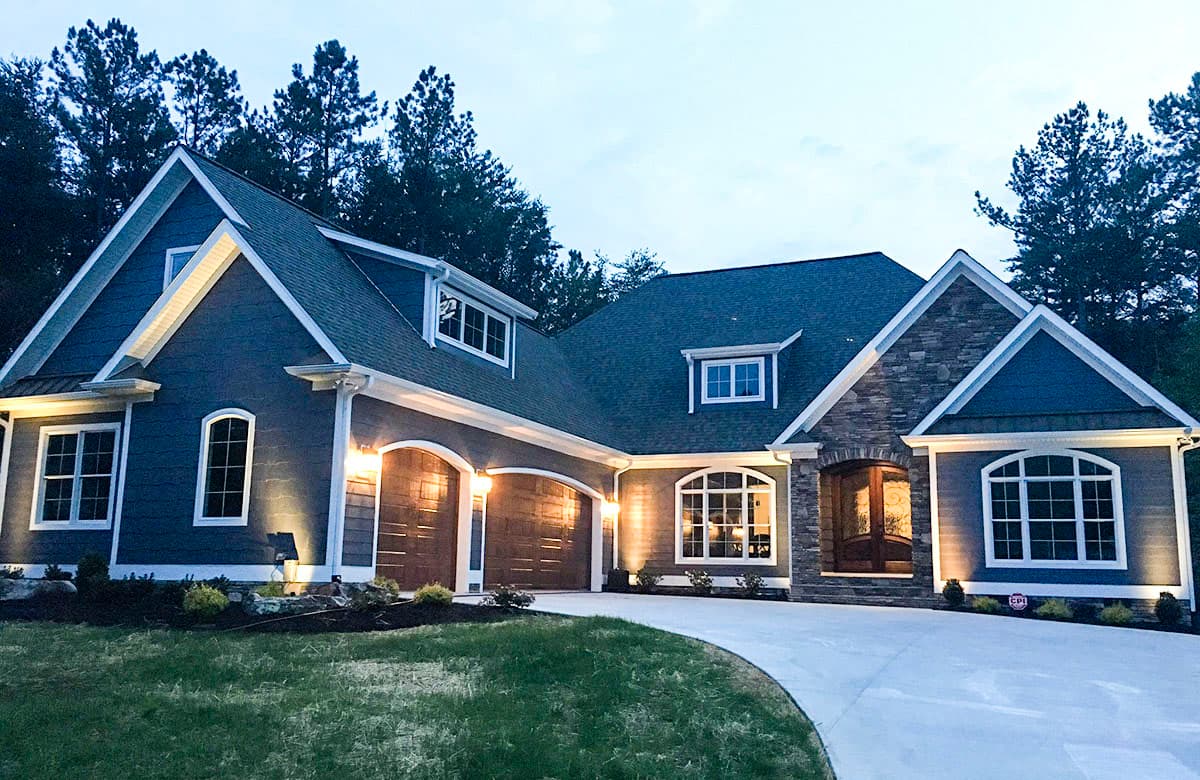 House plan exterior: modern home with stone accents, arched windows, dormers, and a three-car garage.