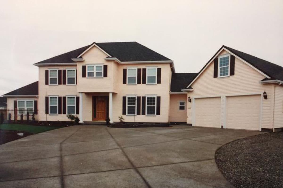 House plan exterior. Two-story Colonial with a detached two-car garage. Features include a front porch, multiple gables, and dark shutters.
