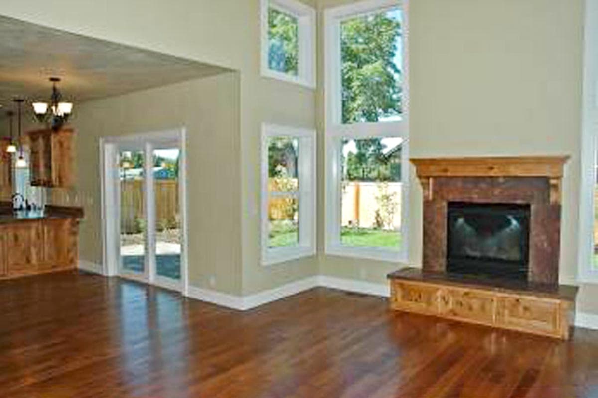 Interior rendering of a living room with a fireplace, large windows, and an open view to the kitchen with wood cabinetry.