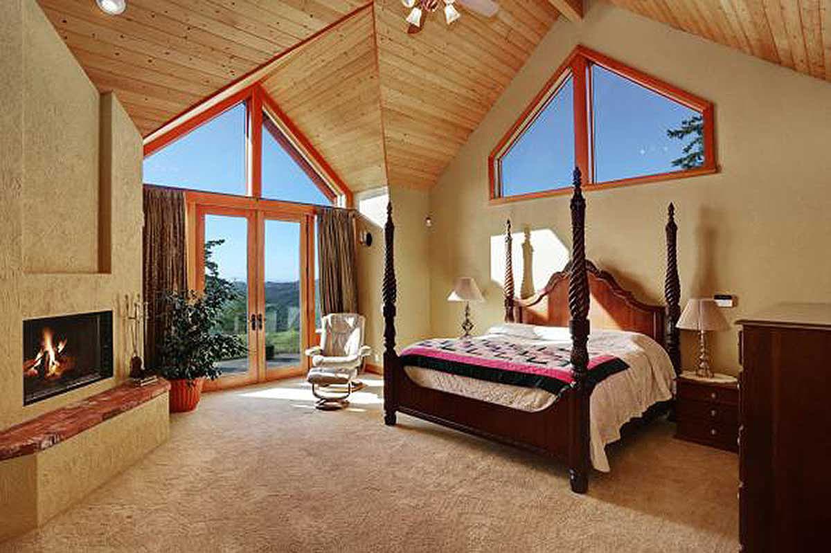 Bedroom with fireplace, four-poster bed, and vaulted wood-paneled ceiling with triangular windows.