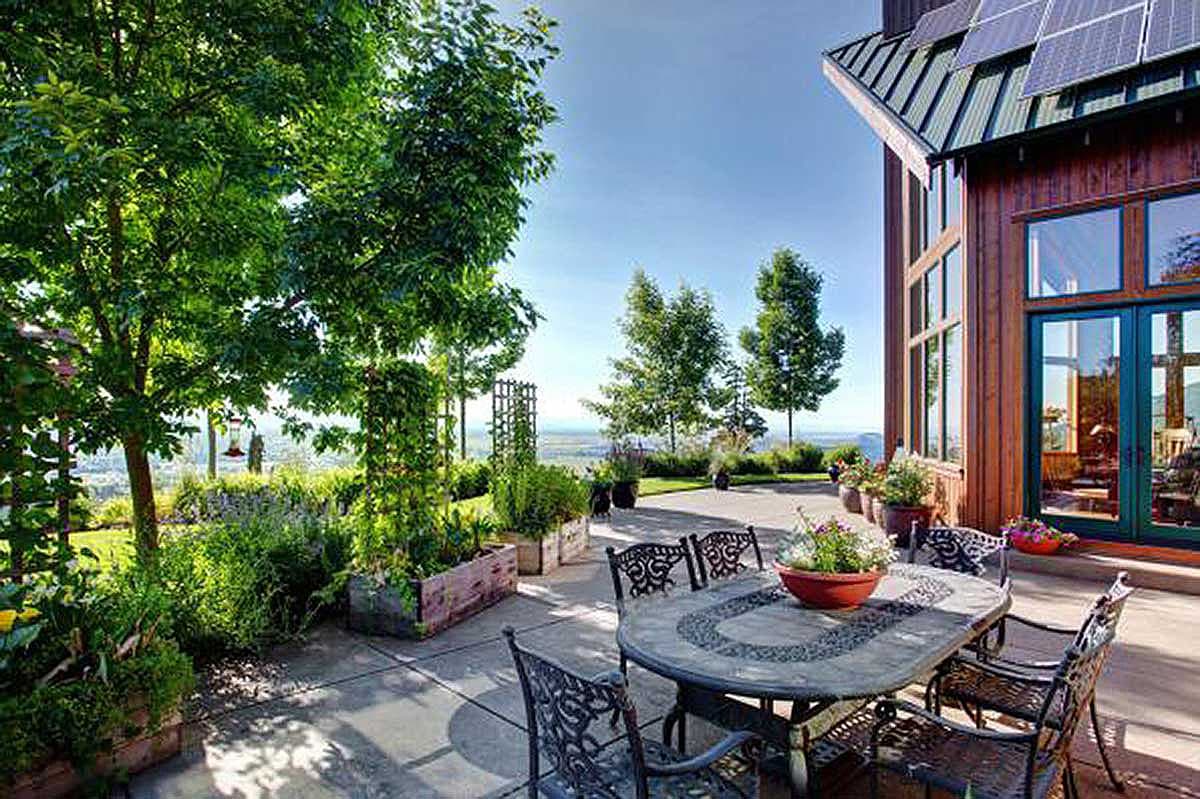 House plan exterior: Modern home with wood siding, solar panels, large windows, and a patio with outdoor dining.