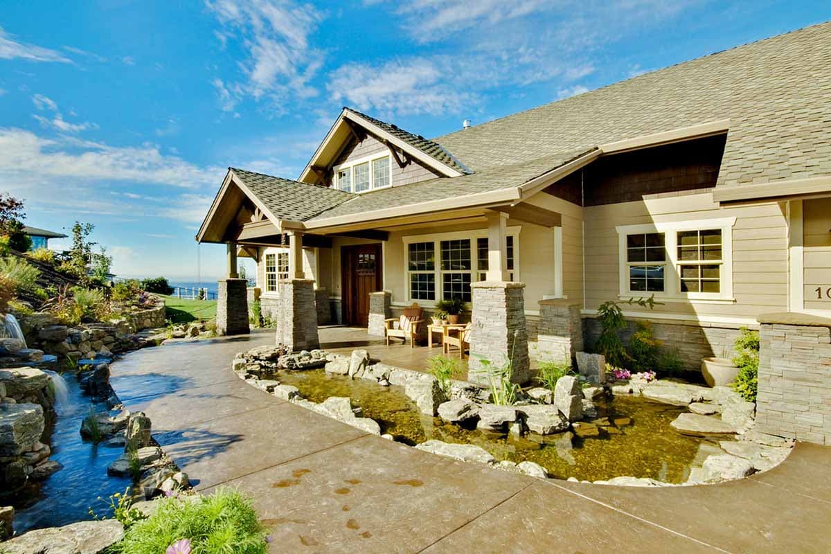 House plan exterior with Craftsman style, covered porch with stone columns, gabled roof, and a water feature. Single story.