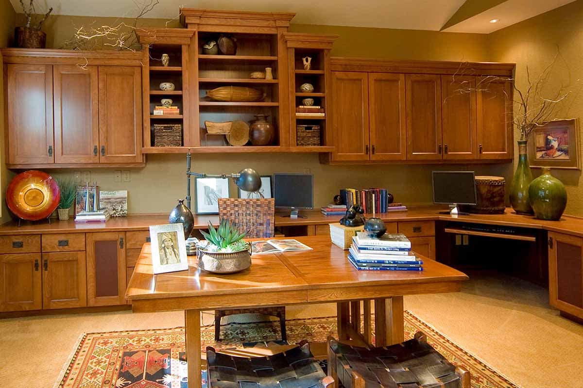 Built-in wooden desk with bookshelves and cabinets, featuring a central table and two workstations.
