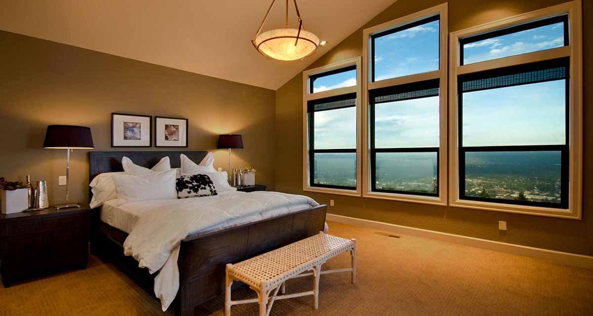 Primary bedroom with vaulted ceiling, dark wood bed, and large casement windows offering panoramic views.