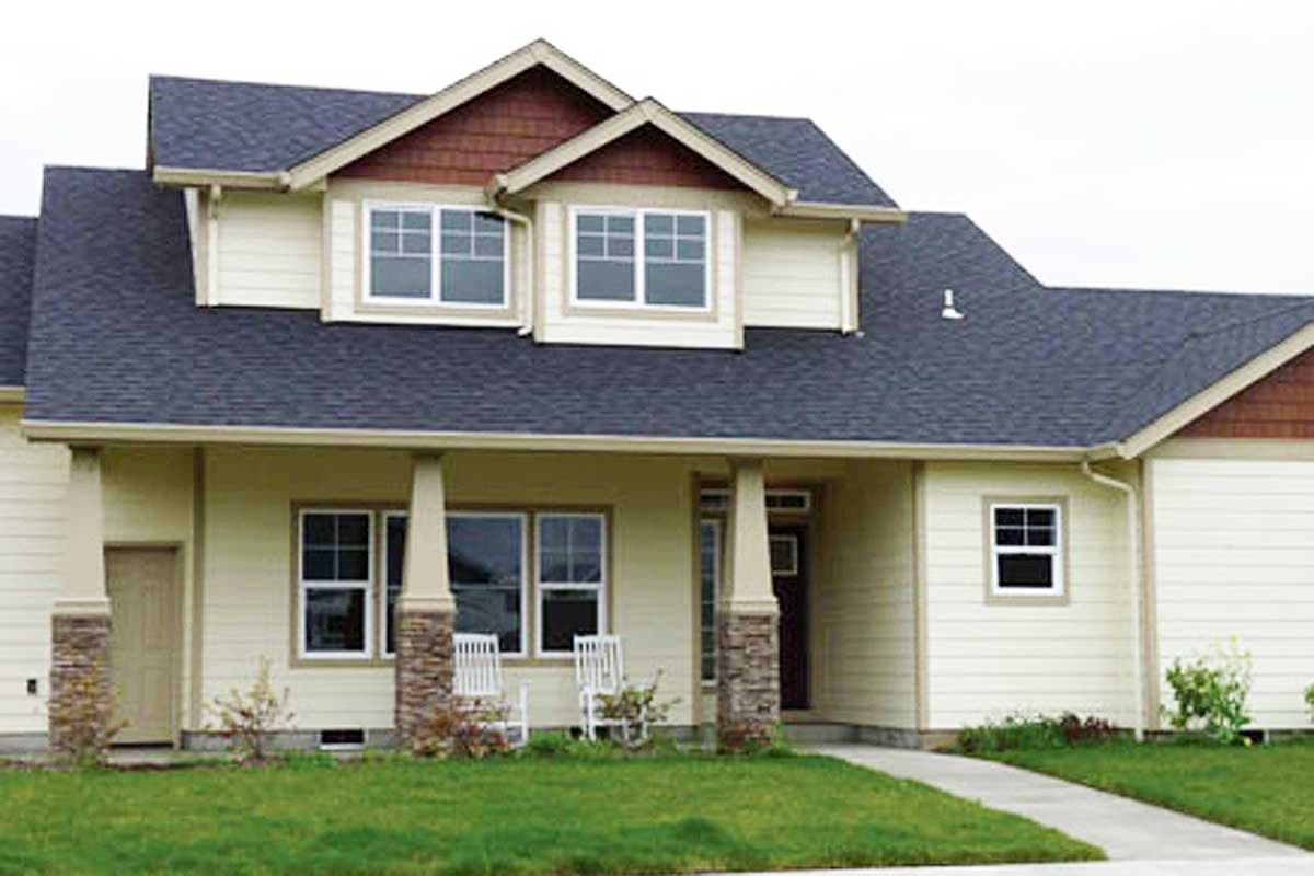House plan exterior with dormers, covered porch supported by stone-clad columns, and multiple gables.