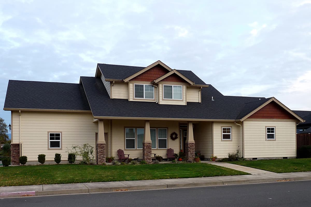 House plan exterior. Two-story home with a porch supported by columns. Features include gables, dormers, and a prominent roofline.