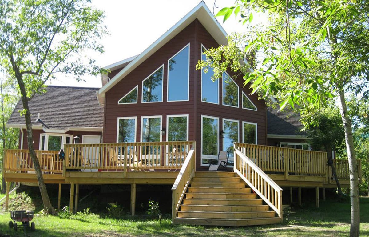 House plan exterior: Modern house with prominent triangular gables, extensive wrap-around deck, and wood siding.