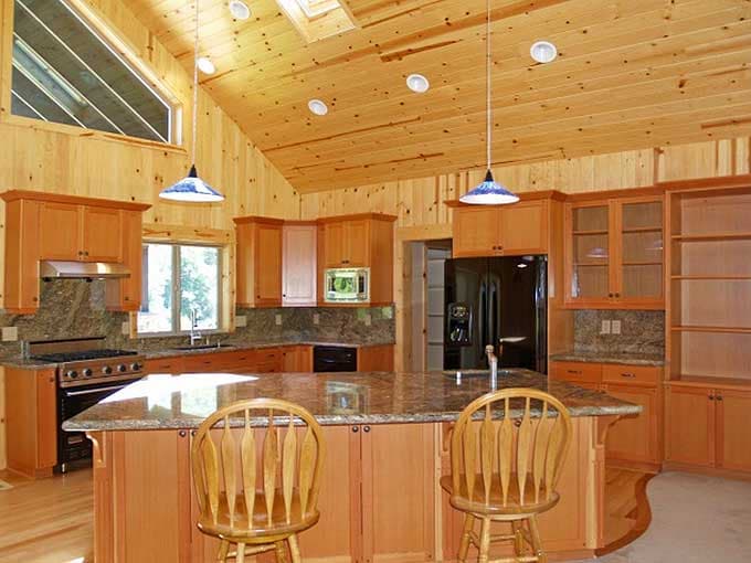 Interior view of a kitchen with a large island, wood-paneled vaulted ceiling, and a triangular window.