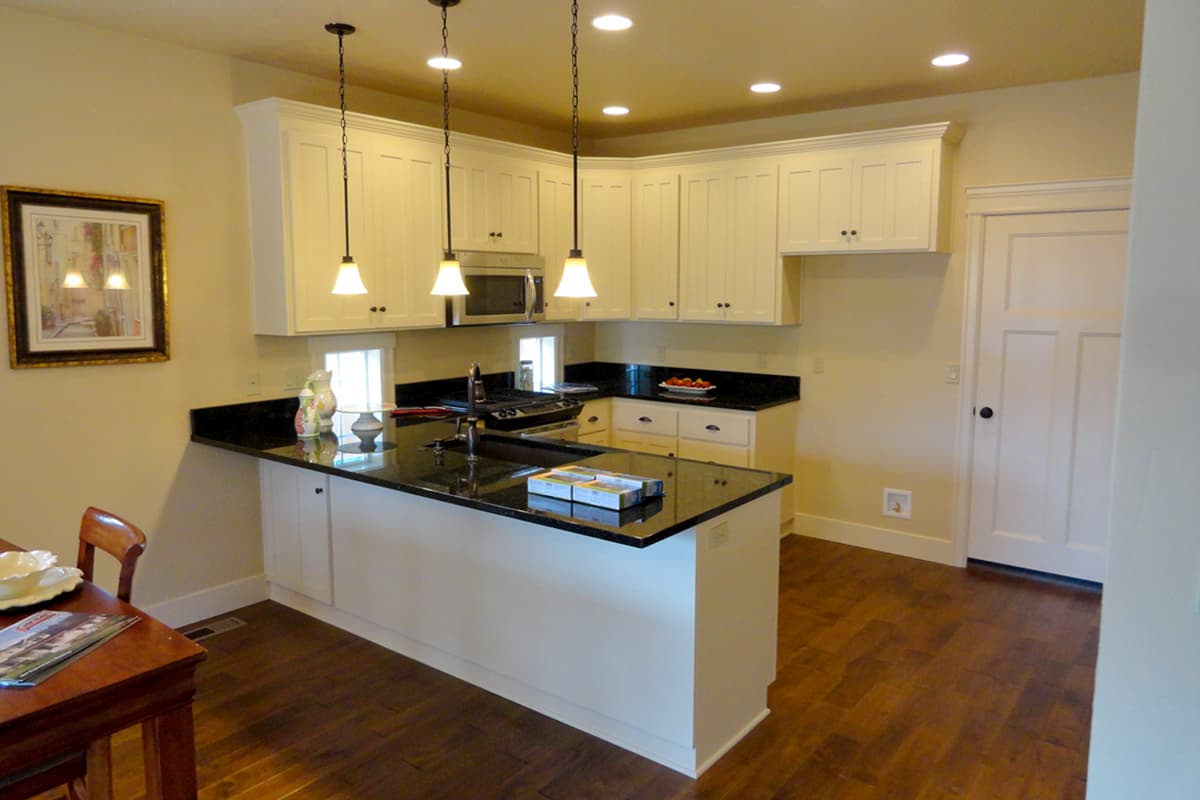 Kitchen with white Shaker cabinets, granite countertops, island with sink, and hardwood floors.
