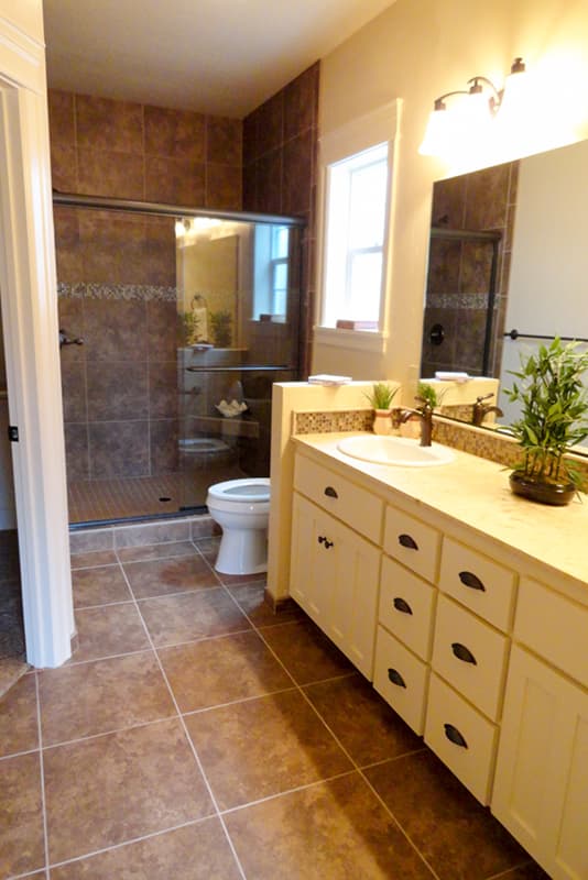 Bathroom with tiled shower, toilet, vanity with double drawers and sink, and a window.