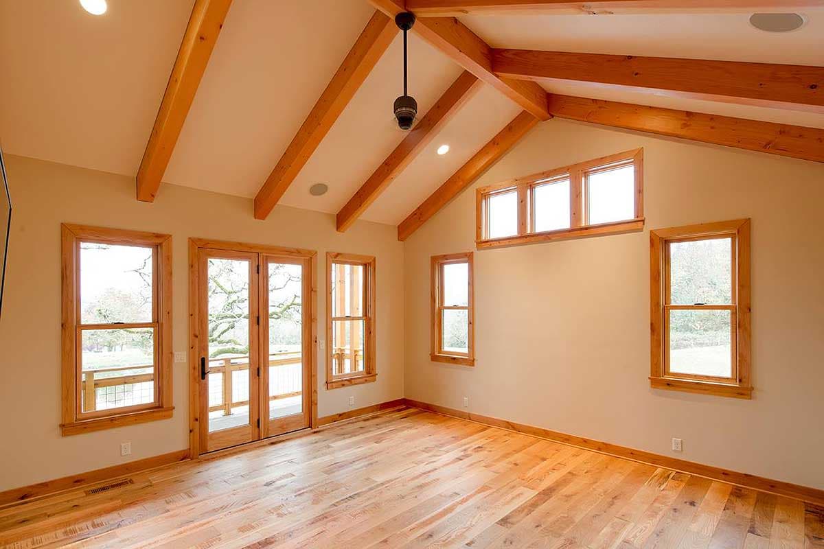 Interior view of a room with vaulted ceilings, exposed wood beams, wood flooring, and multiple windows.