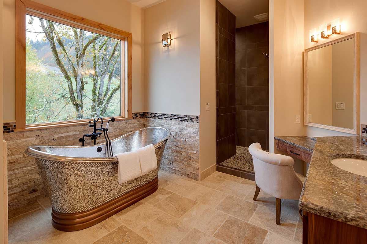 Bathroom with a freestanding tub, large window overlooking trees, walk-in shower with dark tile, and double vanity.
