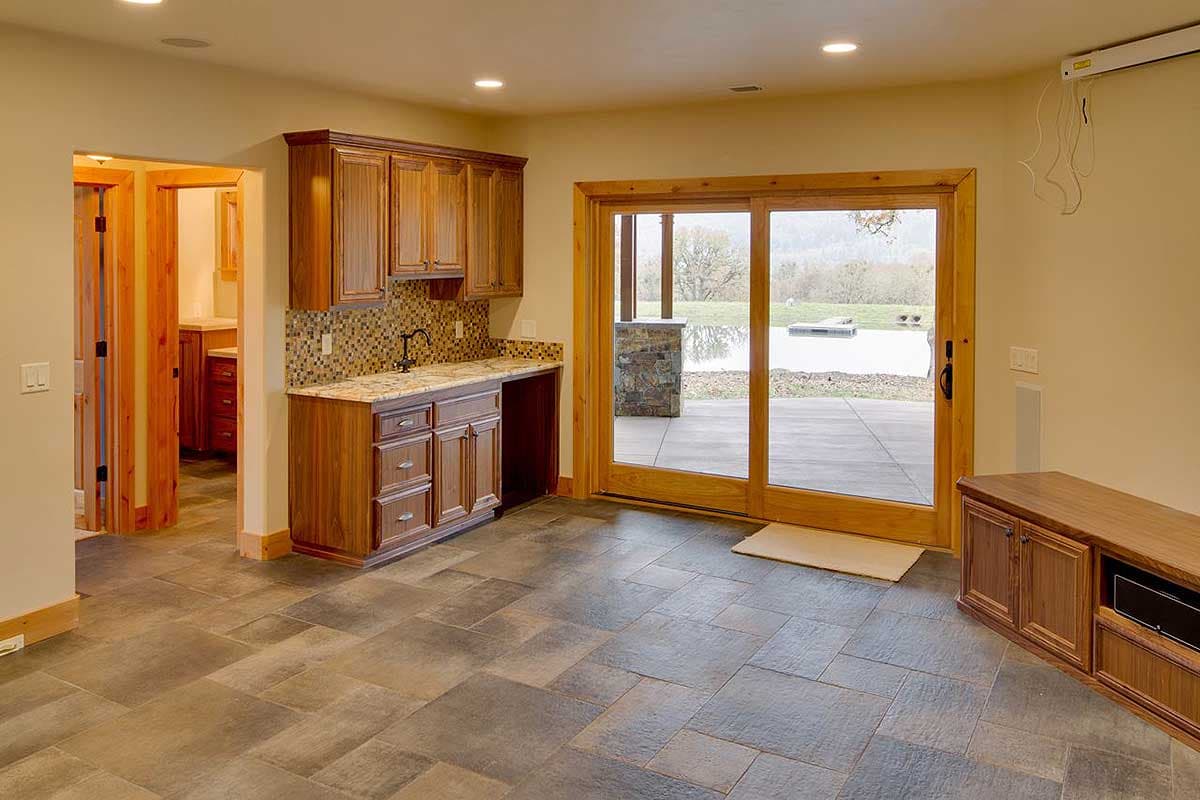 Interior view of a home with a wet bar, wood cabinetry, granite counters, and sliding glass doors leading to a patio with a water view.