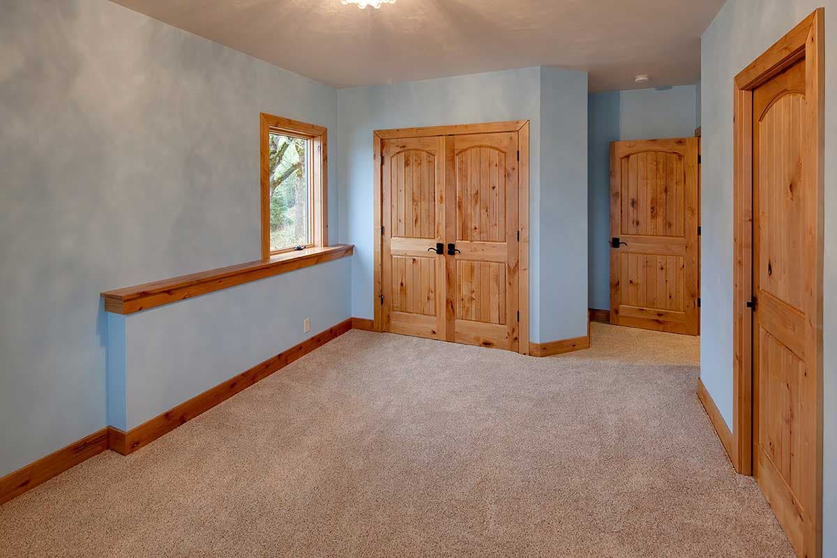 Interior hall with light blue walls, pine doors, and a wooden shelf above a low wall. Carpeted floor.
