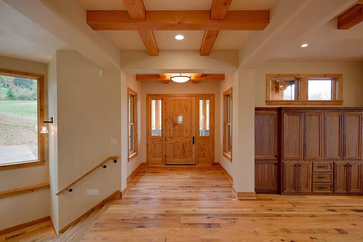Interior view of house entrance with double wood doors, windows, wood beams, and built-in cabinets.