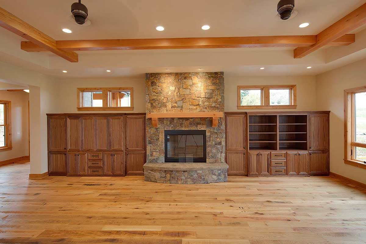 Interior view of a great room with stone fireplace, built-in wood cabinetry, exposed wood beams, and hardwood floors.