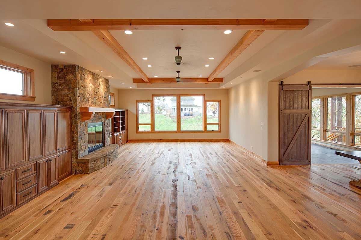 Interior view of great room with stone fireplace, built-in cabinetry, wood beams, and large windows.