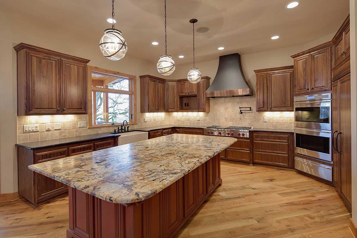 Kitchen with large granite island, dark wood cabinets, stainless steel appliances, and range hood. Rustic wood floors.