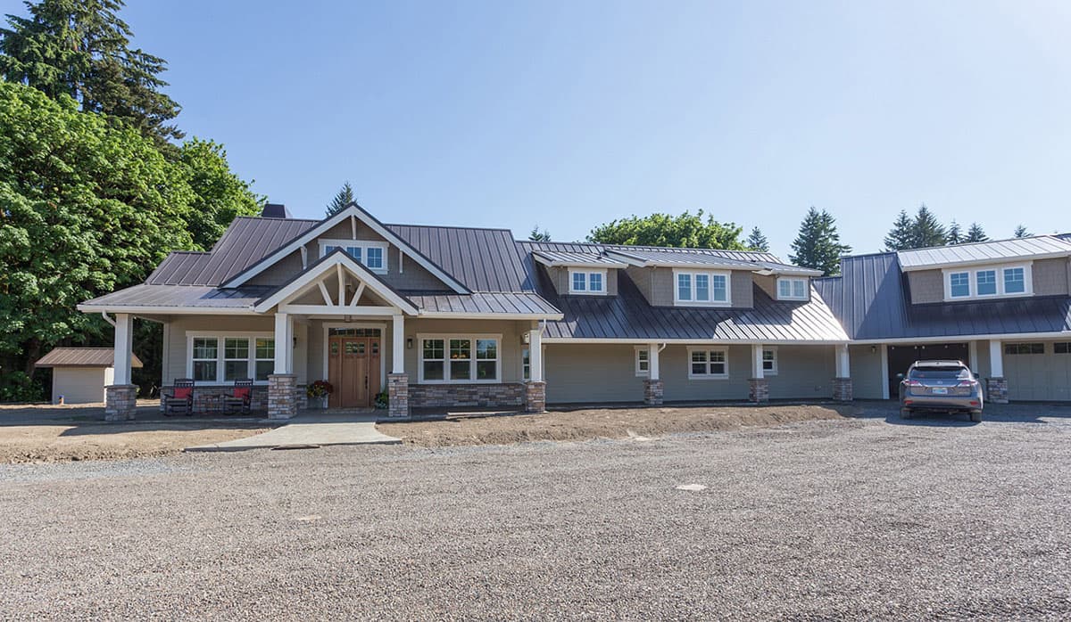 Modern Farmhouse style house plan exterior with metal roof, dormers, covered porch with stone pillars, and a three-car garage.