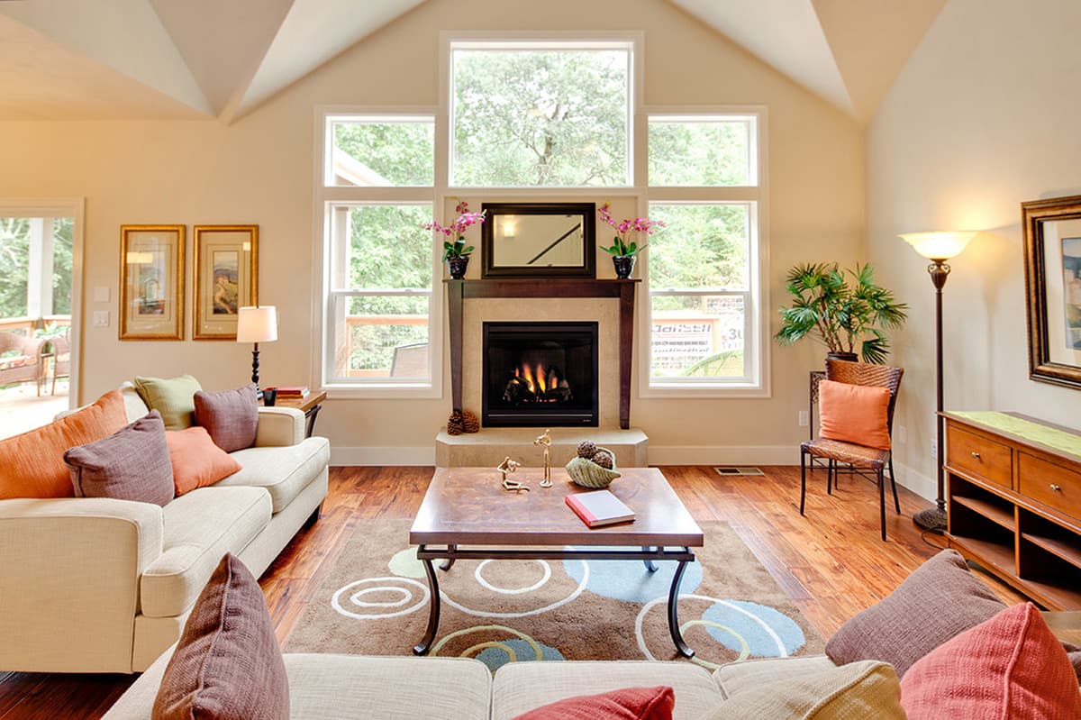 Living room with vaulted ceiling, fireplace, and large windows. Open layout with sofas and coffee table.