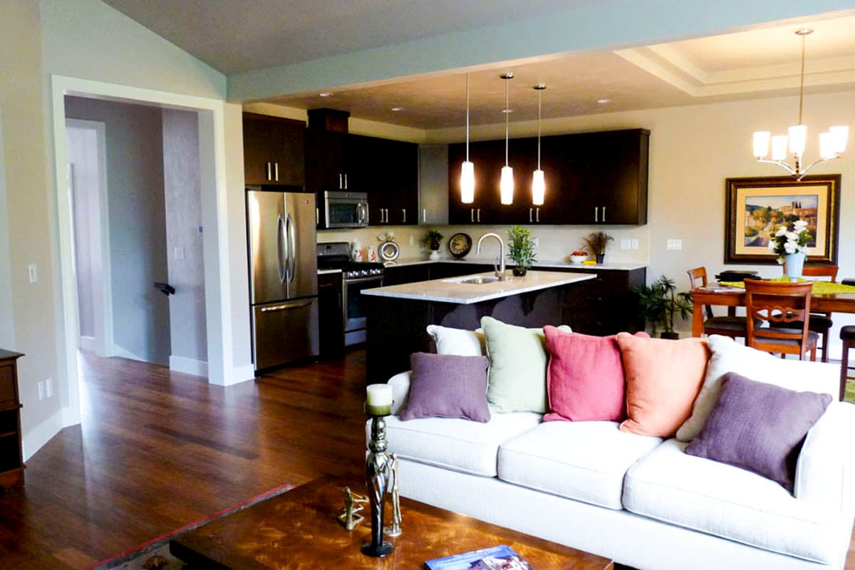 Interior rendering of an open-concept living area with a kitchen island, dark cabinets, stainless steel appliances, and a dining area.