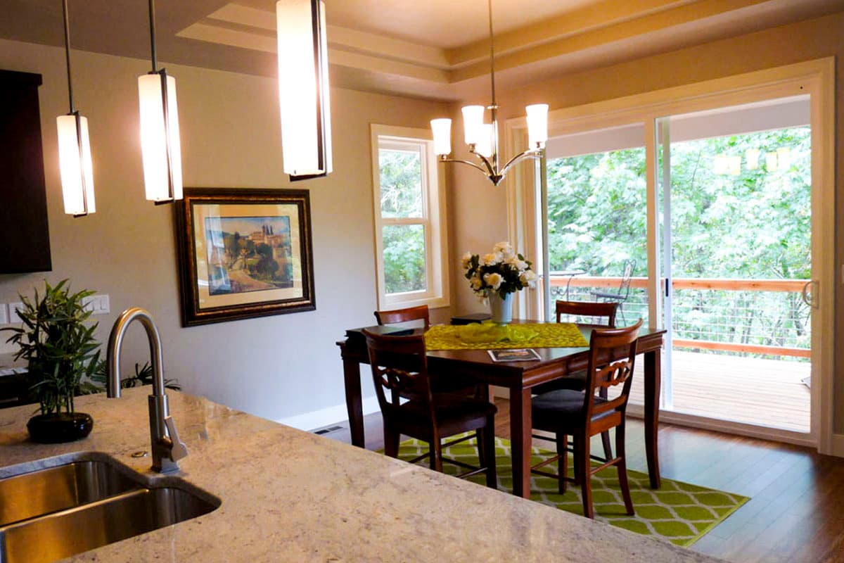 Dining area with table, chairs, chandelier, pendant lights, and sliding glass doors to a deck.