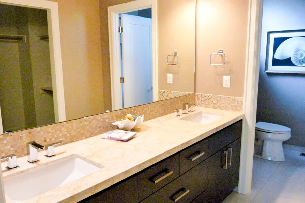 Bathroom with double vanity, dark wood cabinets, beige countertop, mosaic tile backsplash, and a toilet.