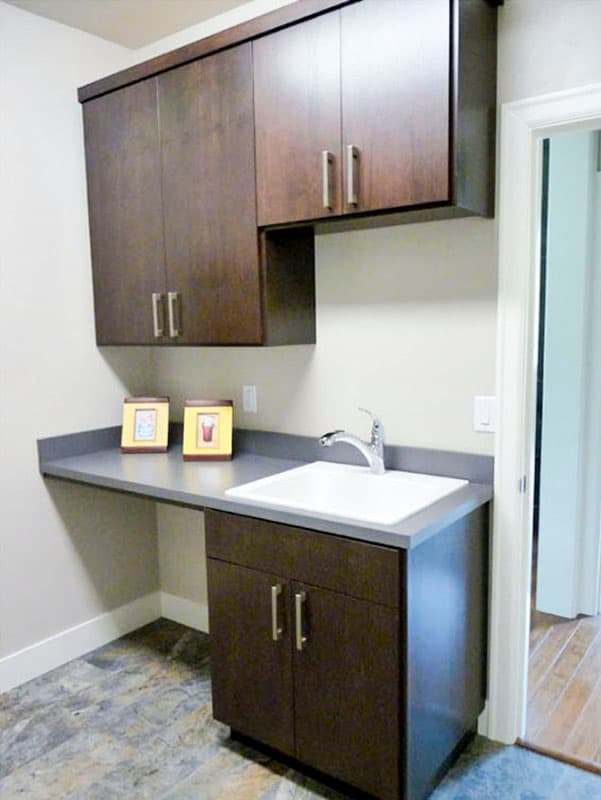 Laundry room with dark wood cabinetry, a sink, countertop workspace, and tile flooring.