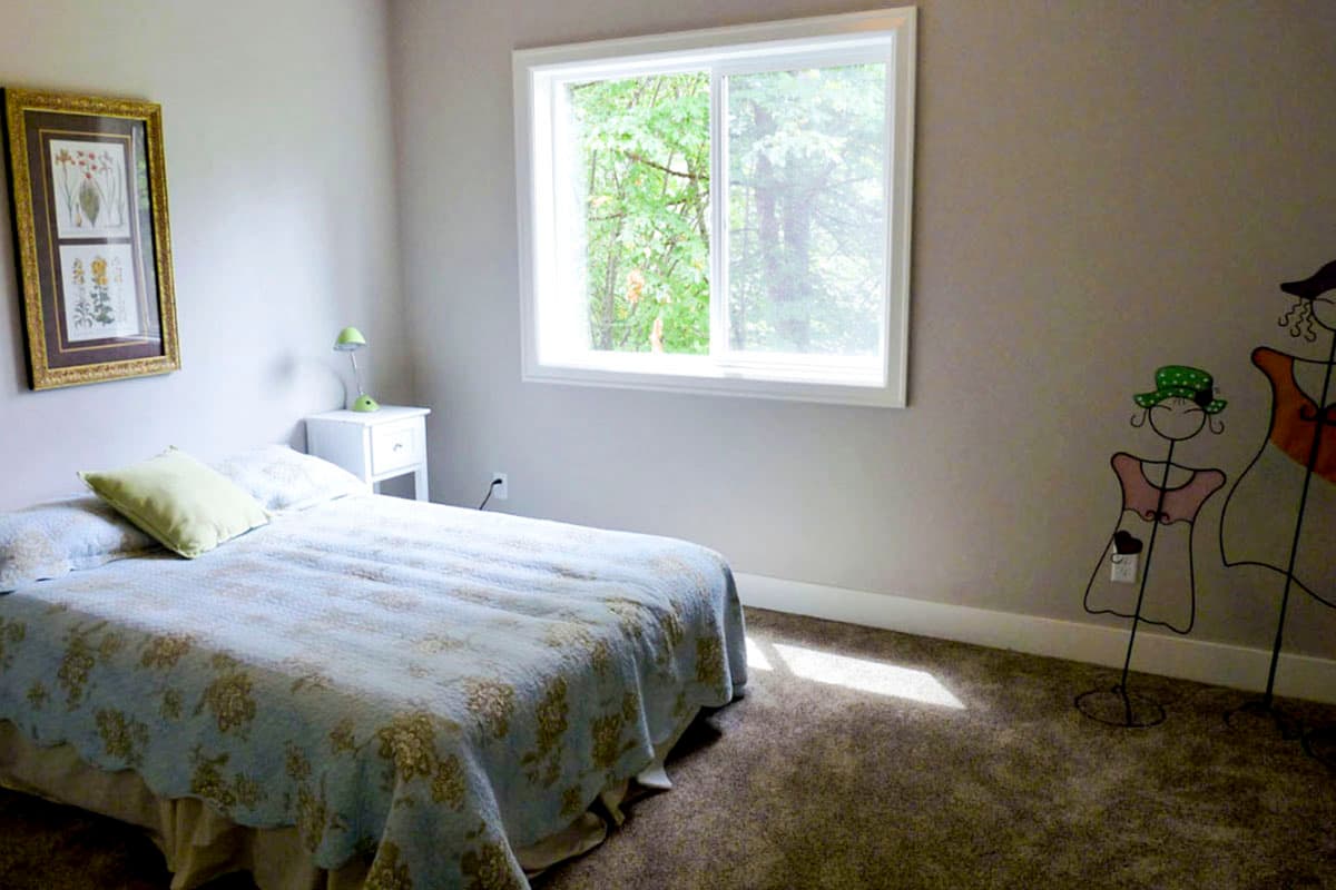 Bedroom interior with a queen bed, nightstand, large window, and decorative wire figures.