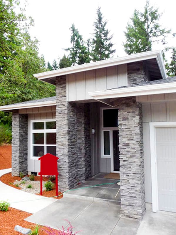 Modern house plan exterior with stone-clad columns, gable roof, wide soffits, and prominent window.