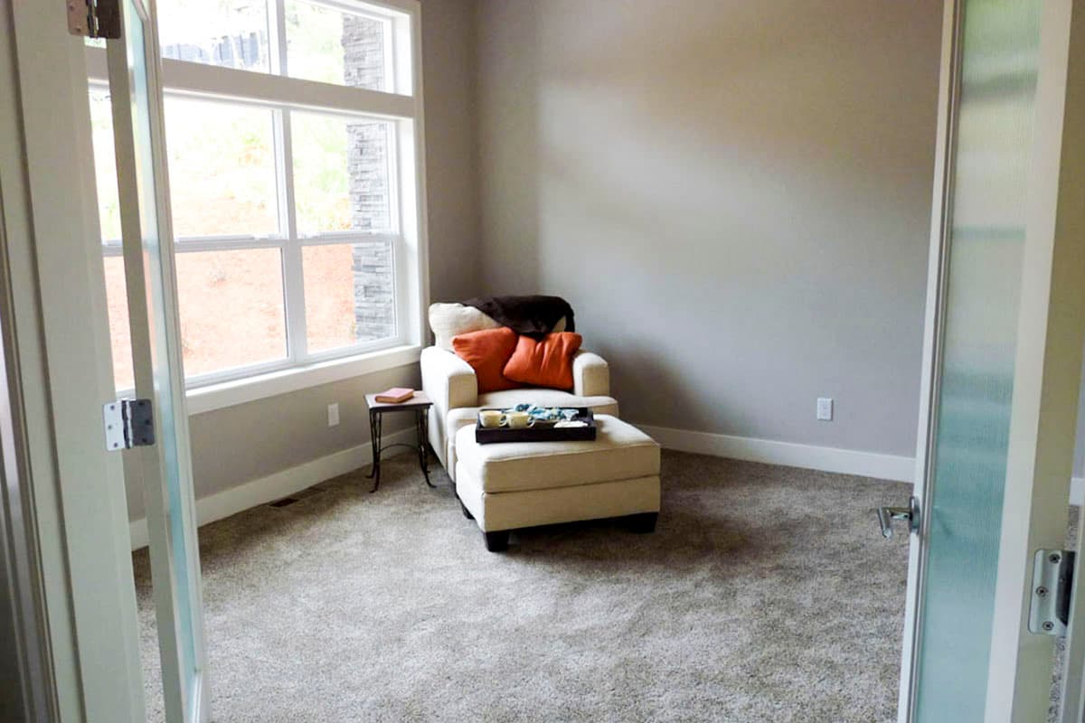 Interior view of a room with a chair, ottoman, and large windows with stone accents.