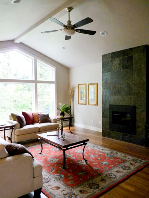 Living room with vaulted ceiling, large corner fireplace, and a sectional sofa facing a coffee table and ornate rug.